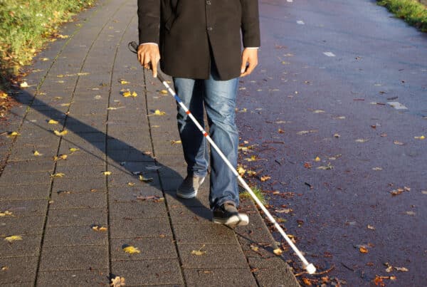 Person using white cane walking along sidewalk