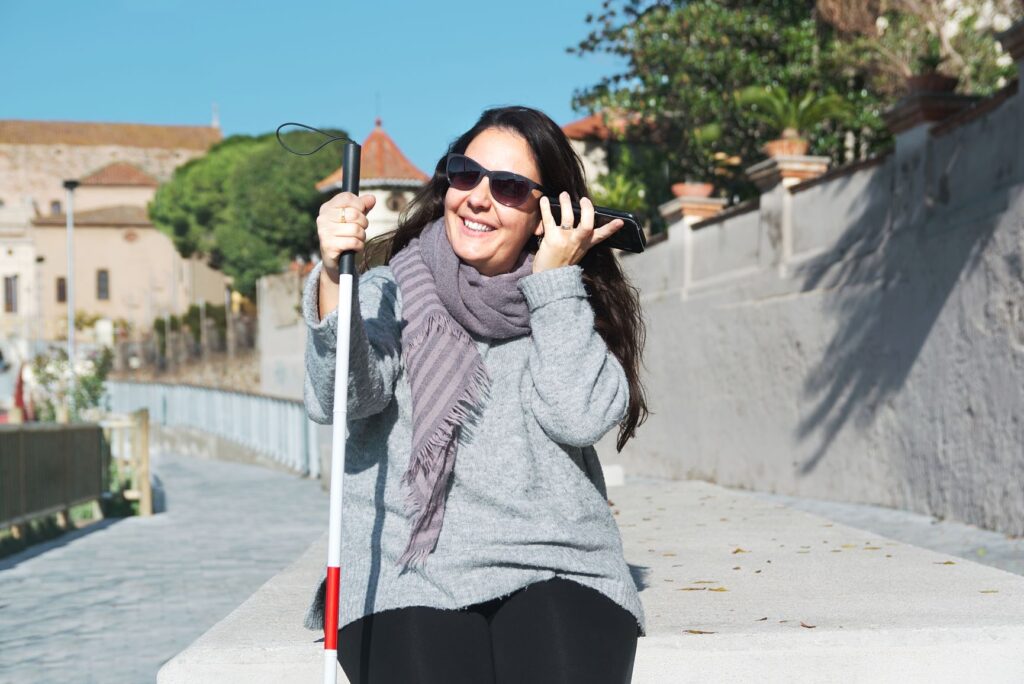 Young woman sitting with her white cane and listening to her smartphone