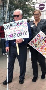 Bill and Judy walking in white cane day march holding signs.