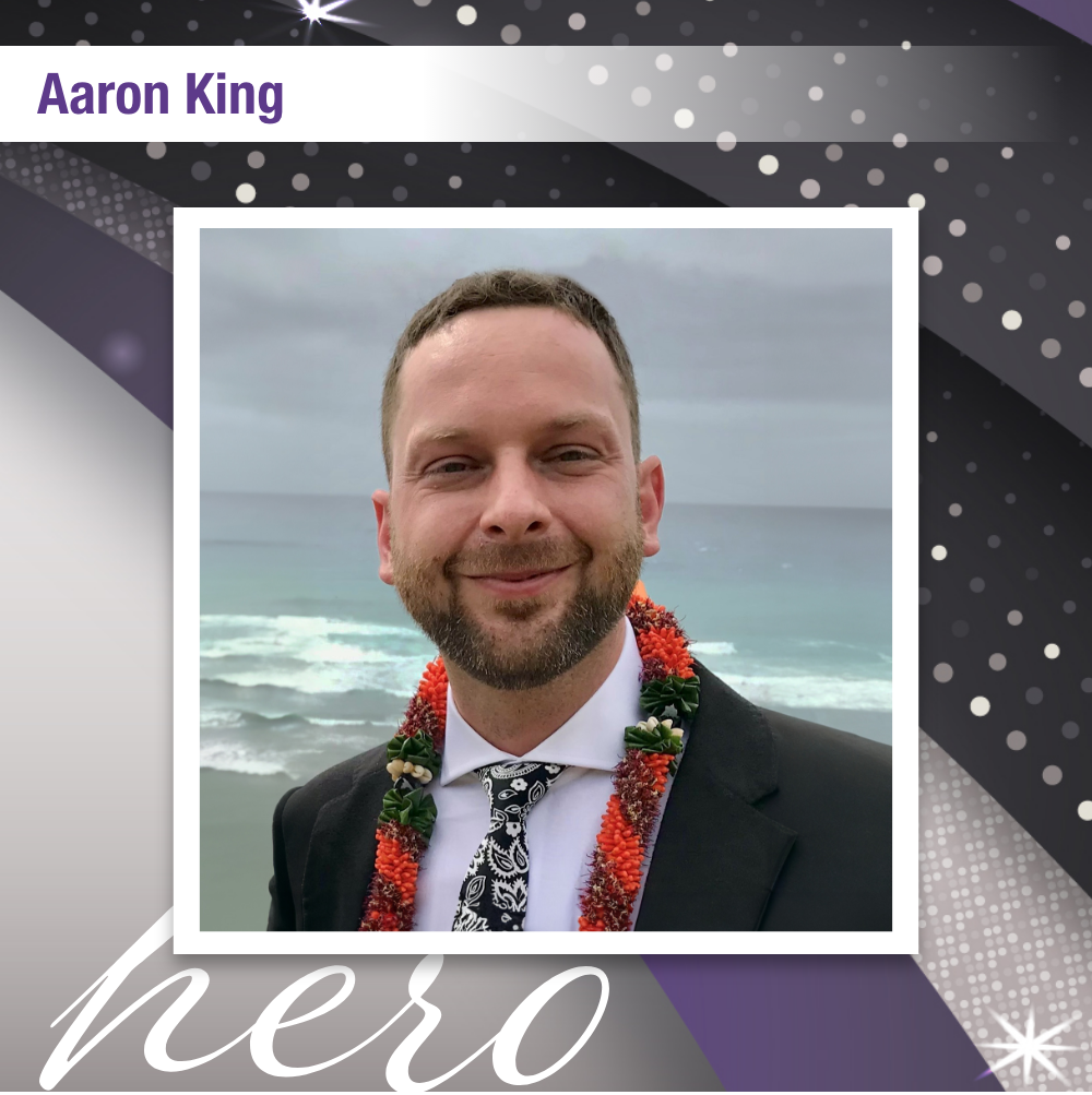 Photo of Aaron King that reads "hero". He is wearing a tuxedo and a Hawaiian lei smiling in front of the ocean.